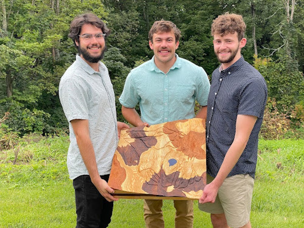 The three founders of Treeline Terrains hold up a topographic carving of Middlebury's Snow Bowl.